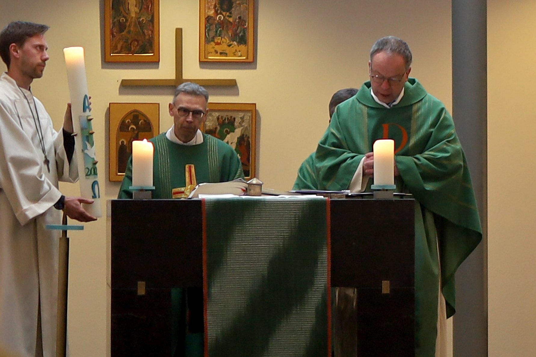 Pastoralreferent Jonas Sträßer (links) hält die Osterkerze, die durch Pfarrer Lars Krüger (rechts) übergeben wird. 