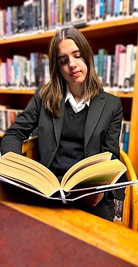 Carla Schadow liest in der Bibliothek aus einem dicken Buch.