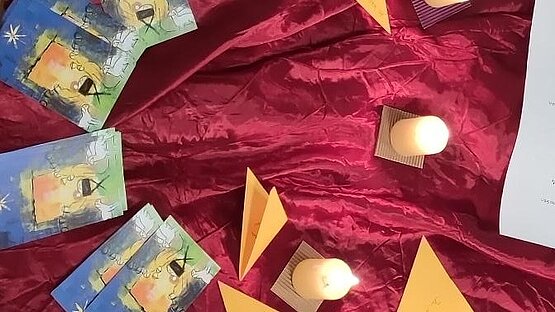 auf den Boden gelegtes rotes Tuch mit Kerzen, Notizen und Postkarten 