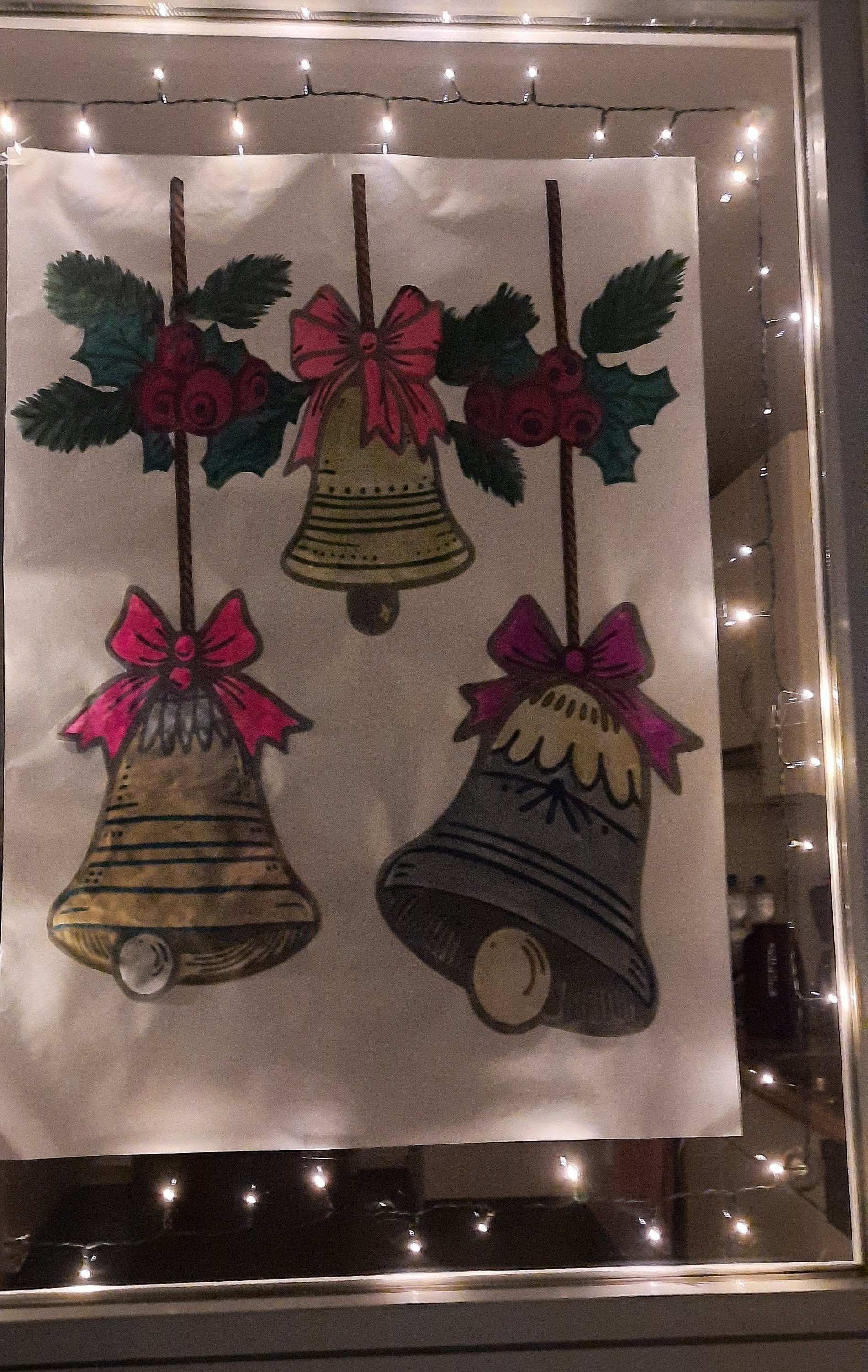 Mit Folienpapier gestaltete Glocken an einem beleuchteten Fenster.