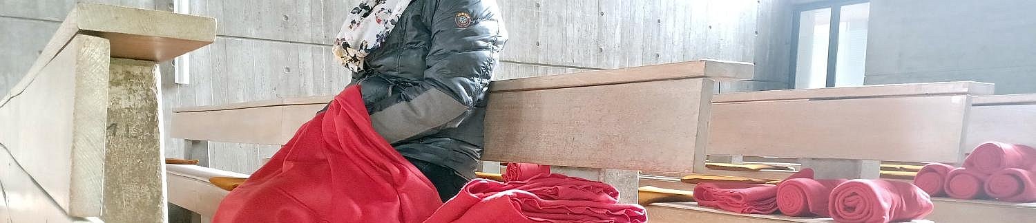 Gottesdienstbesucherin mit Decke über den Knien.