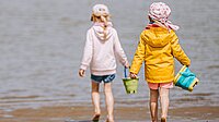 Zwei Kinder mit Eimern laufen über den Strand in Richtung Meer.