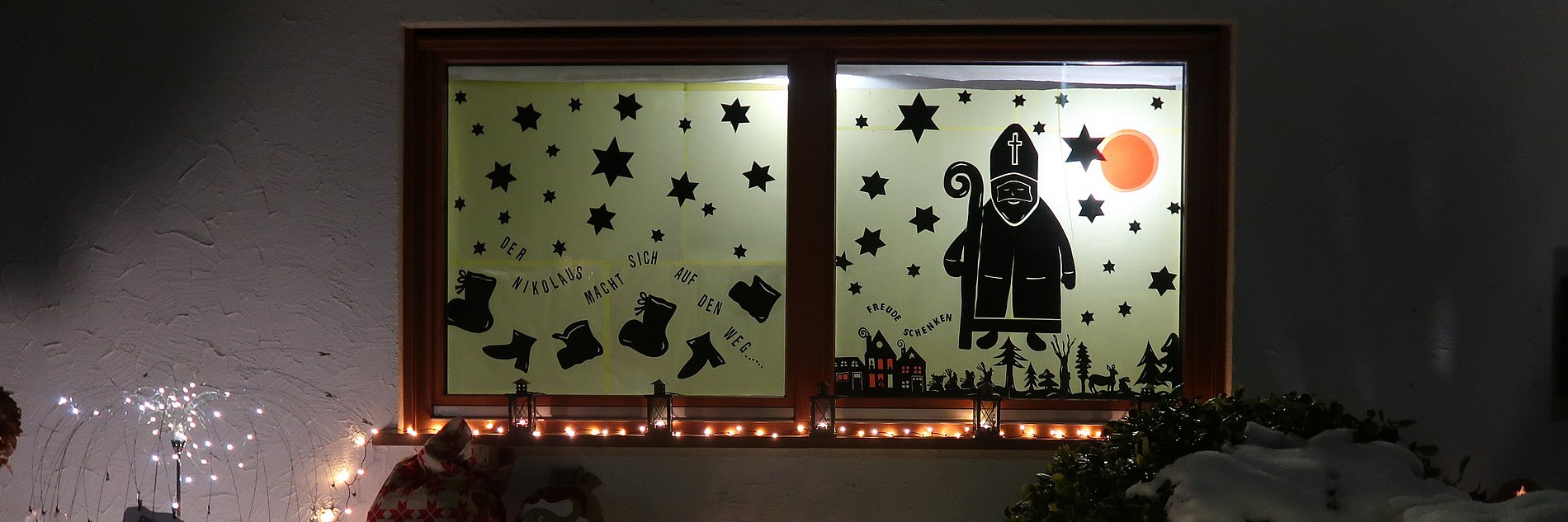 Mit dem Nikolaus und Weihnachtssymbolen beklebtes Adventsfenster.