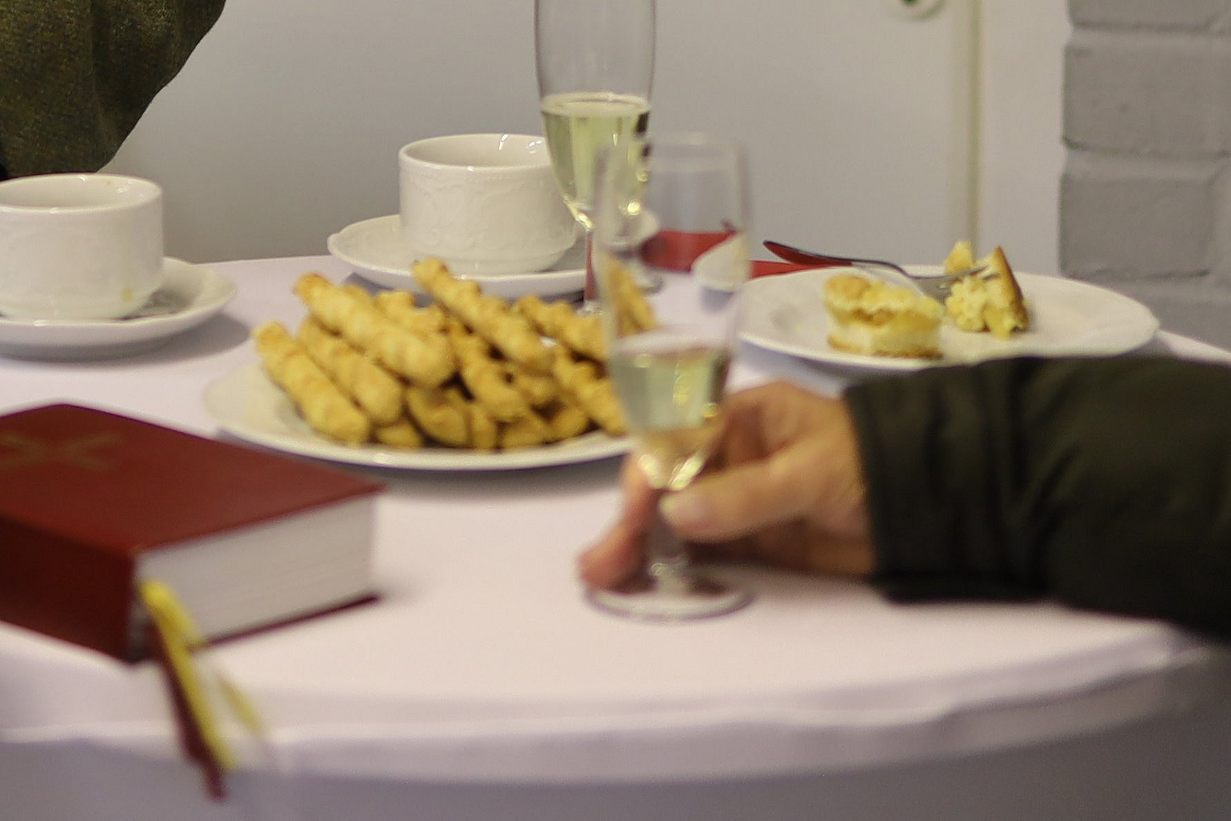 An einem Stehtisch wird Kaffee, Sekt und Gebäck serviert. Eine Bibel liegt auf dem Tisch. 