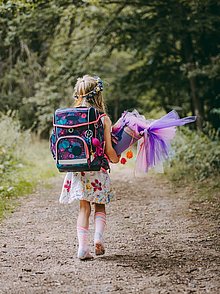 Ein Mädchen läuft mit seiner Schultüte und Schulranzen einen Weg im Wald.