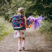 Ein Mädchen läuft mit seiner Schultüte und Schulranzen einen Weg im Wald.