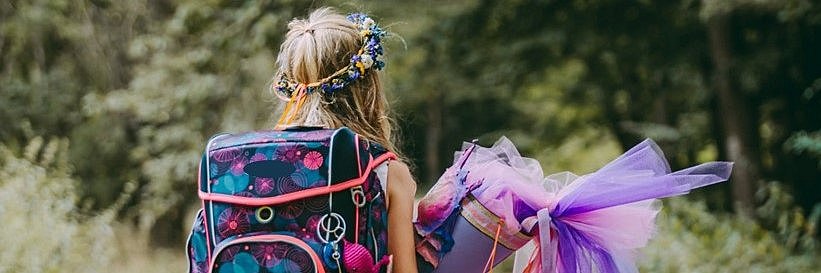 Ein Mädchen läuft mit seiner Schultüte und Schulranzen einen Weg im Wald.