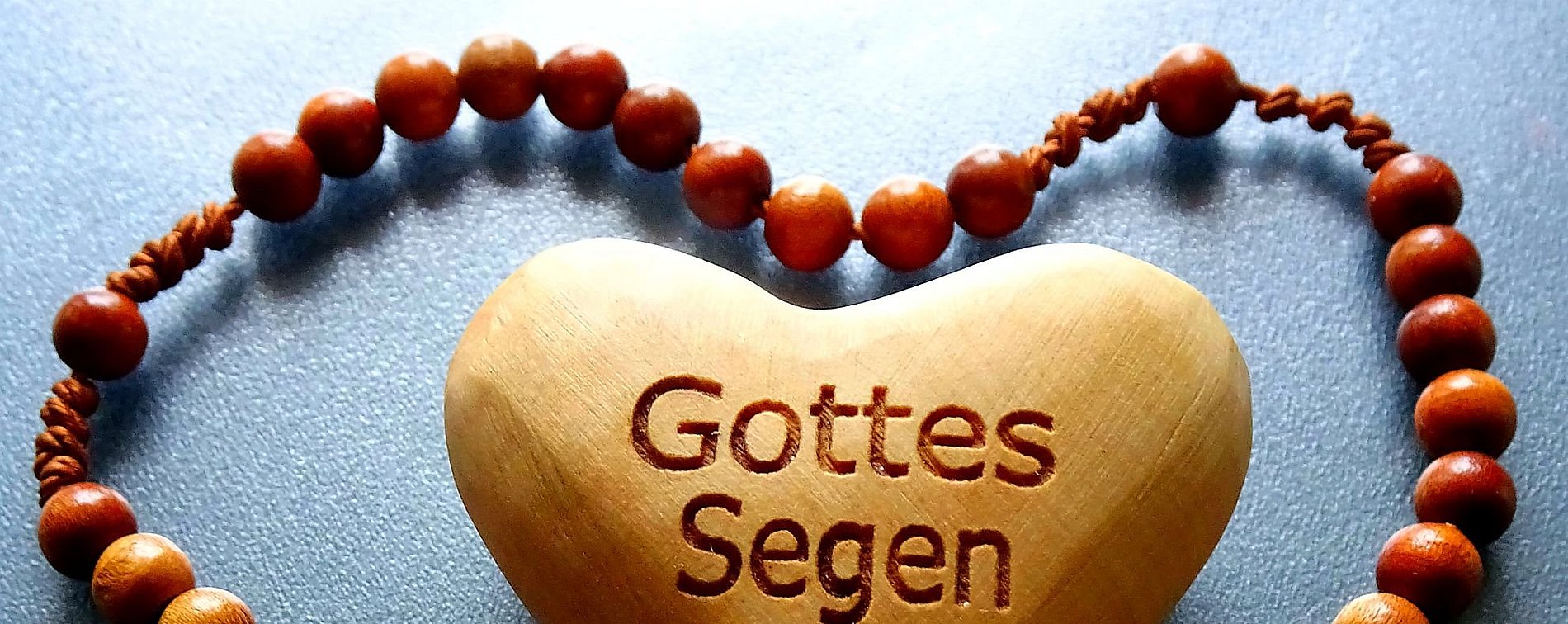 Eine Kette aus Holzperlen umschließt in Herzform ein Herz aus Holz, mit der Aufschrift "Gottes Segen"