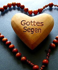 Eine Kette aus Holzperlen umschließt in Herzform ein Herz aus Holz, mit der Aufschrift "Gottes Segen"