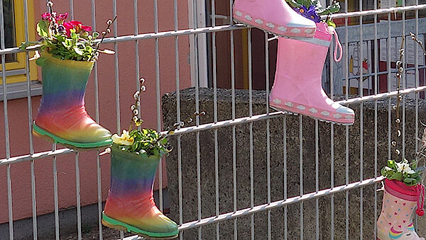Upcycling von Gummistiefeln: Die Kita-Kinder bepflanzen die farbenfrohen Blumentöpfe und verschönern den Zaun.